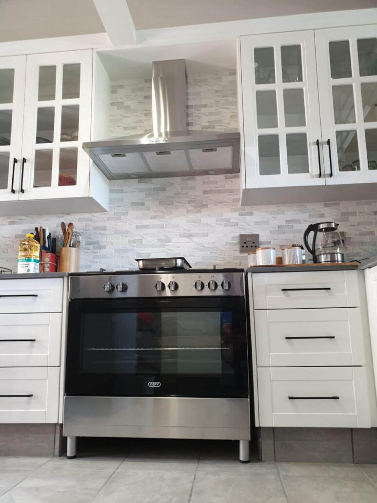 Modern white kitchen renovation in Johannesburg featuring a stainless steel Defy oven, marble subway tile backsplash, and shaker-style cabinets.