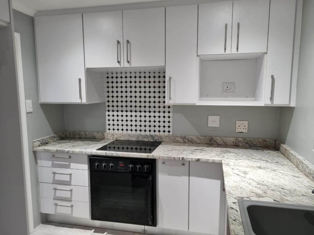 Small kitchen renovation with granite countertops, a black built-in oven, and a classic black and white circular mosaic tile backsplash.