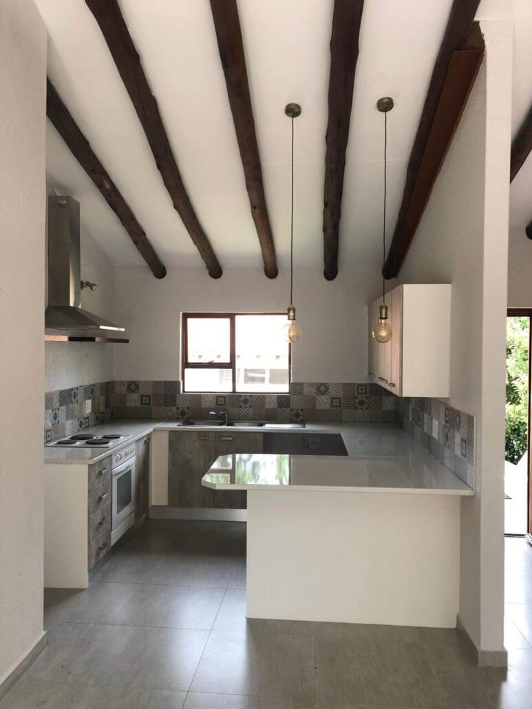 Rustic kitchen remodel featuring exposed dark wood ceiling beams, white quartz countertops, and decorative patterned backsplash tiles.