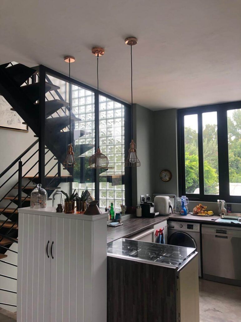 Industrial-style kitchen renovation with copper pendant lighting, a black metal staircase, and a glass block feature wall.