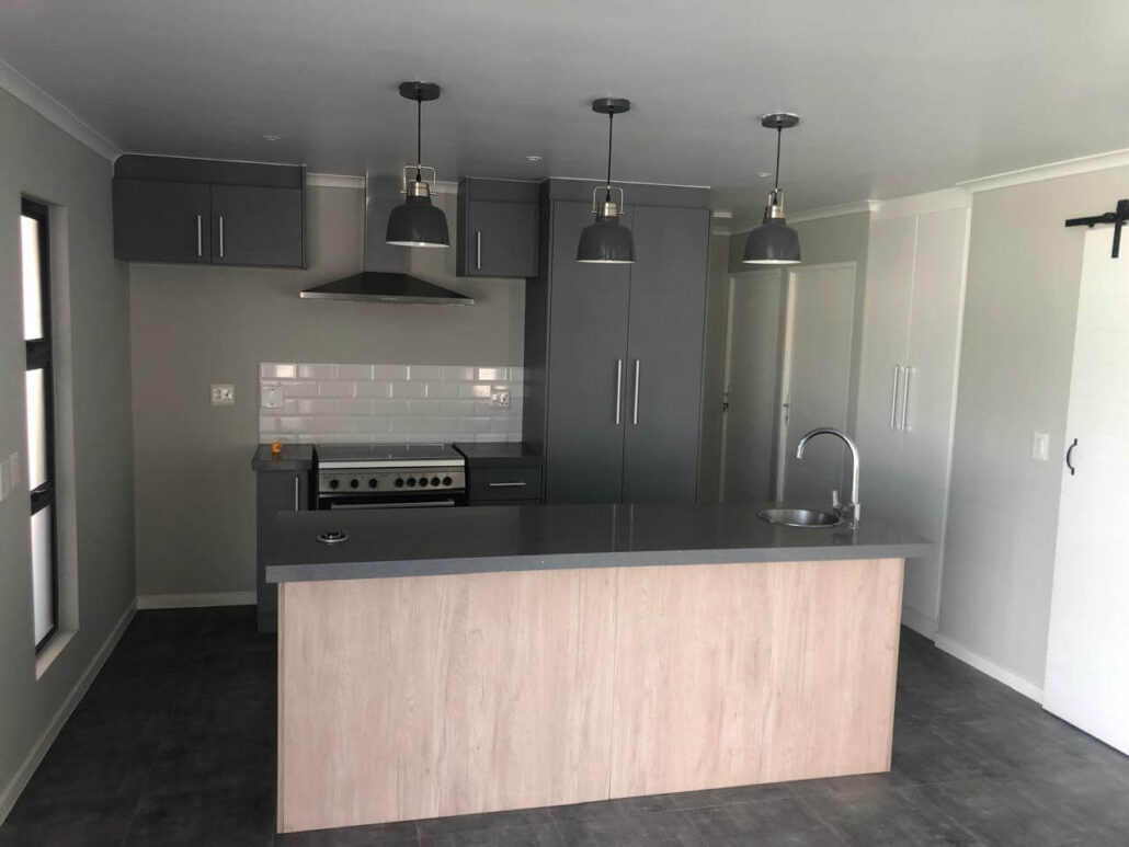 Two-tone kitchen renovation featuring charcoal grey cabinetry, a light wood island, and black industrial pendant lights.