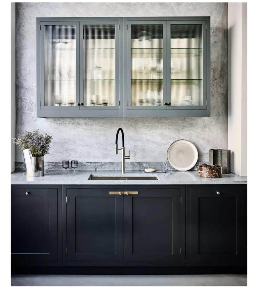 Contemporary kitchen featuring fluted glass upper cabinets, matte black lower cabinetry, and a grey marble backsplash with a gooseneck faucet.