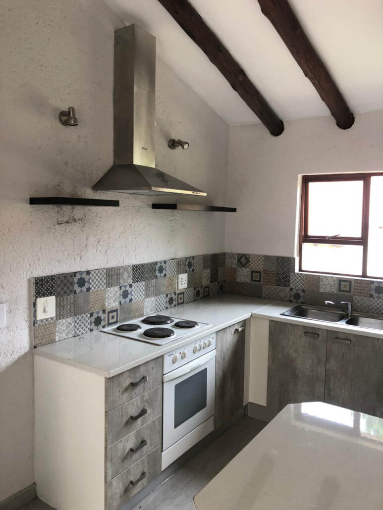 L-shaped kitchen design with grey wood-grain cabinets, a white gas stove, and Mediterranean-style mosaic backsplash tiles.