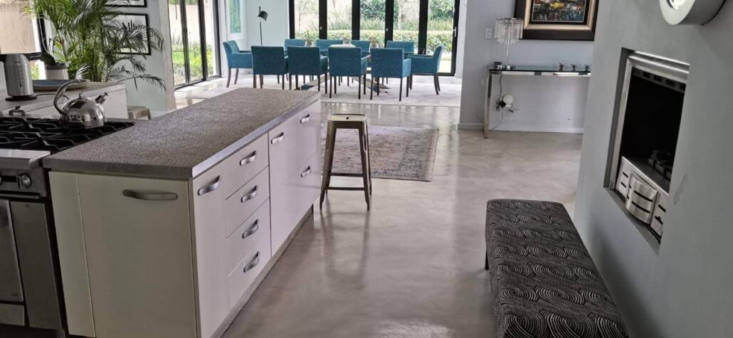 Open-plan kitchen and dining area remodel with polished concrete floors, a large central island, and modern blue dining chairs.